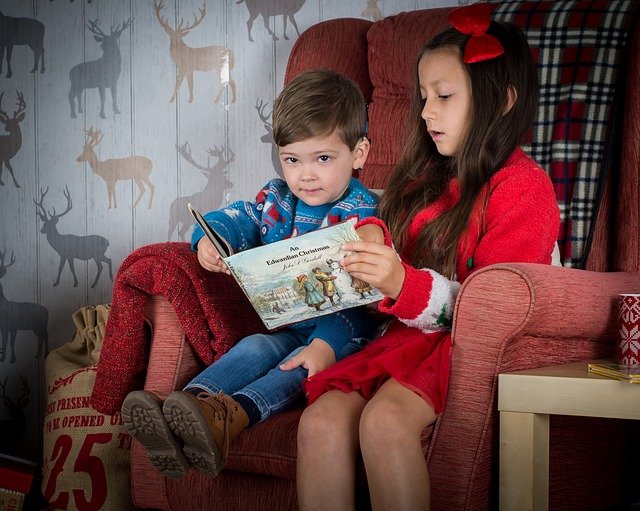 Little girl reading a Christmas book to her little brother 